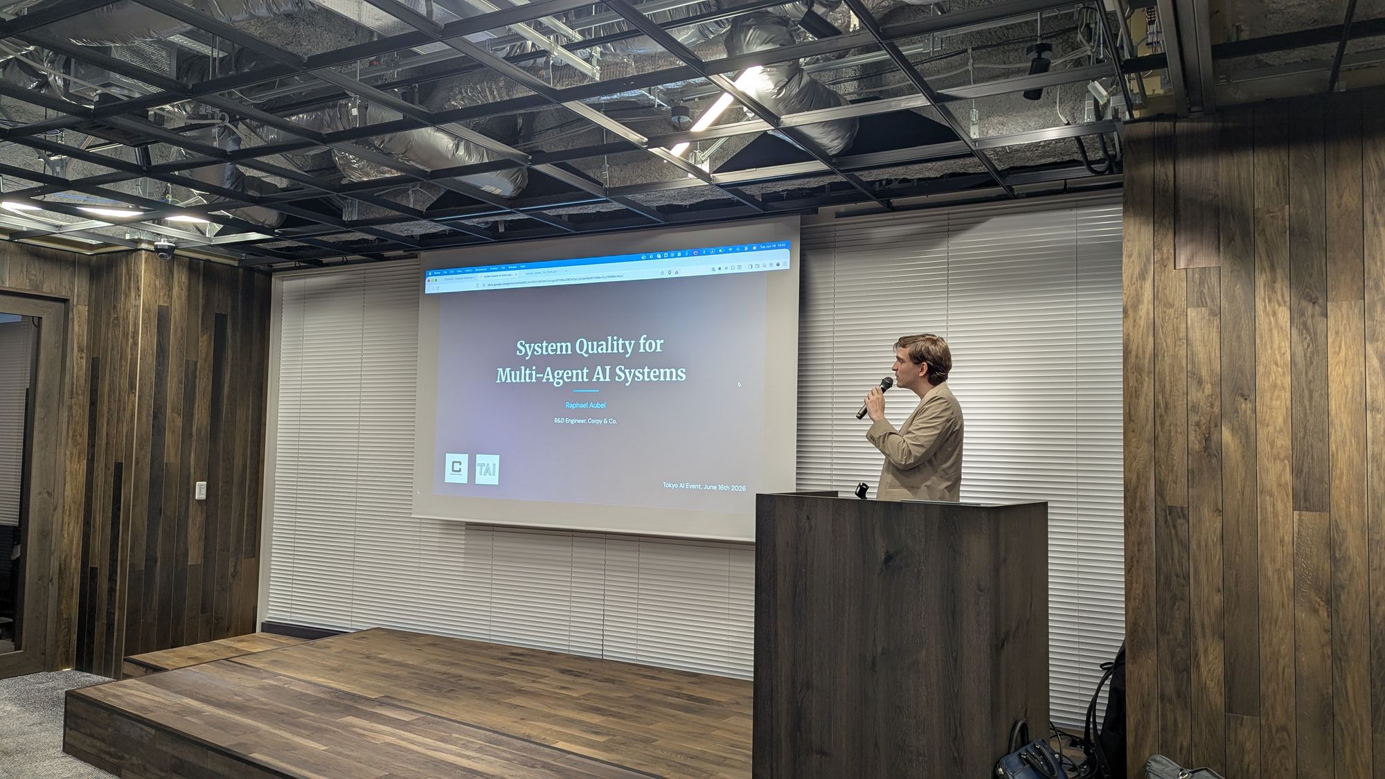A speaker at a lectern beside the title slide System Quality for Multi-Agent AI Systems.