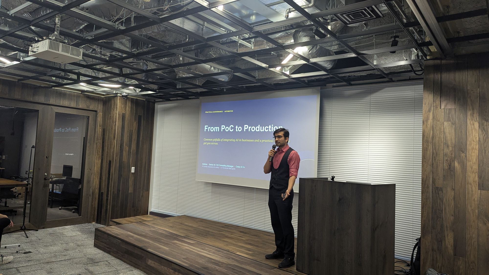 A speaker on stage beside a slide titled From PoC to Production.